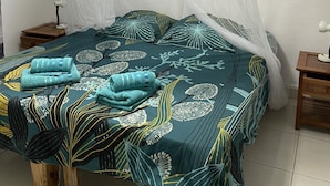 A bedroom with a bed covered by a mosquito net, a bedside table, and a nightstand.
