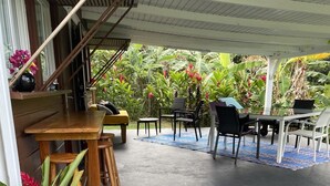 An outdoor patio with wooden tables and chairs, surrounded by lush greenery and tropical plants.
