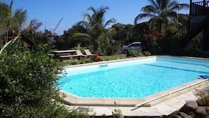 A rectangular swimming pool with clear blue water, surrounded by rocks and greenery.