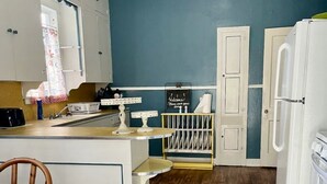 A kitchen with a wooden floor, white cabinets, a central island with stools, and a refrigerator. - Garden Cottage in the city. (West Monroe)