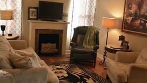 A living room with a fireplace, a television, and a green armchair. - Garden Cottage in the city. (West Monroe)
