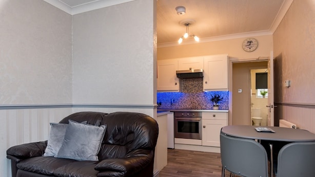 A compact living space with a leather sofa, a small dining table, and a kitchenette in the background. - Cattle Market View Apartment (Boston)