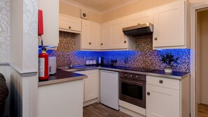 A kitchen with white cabinets, a blue-tiled backsplash, a stainless steel range hood, and a white dishwasher. - Cattle Market View Apartment (Boston)