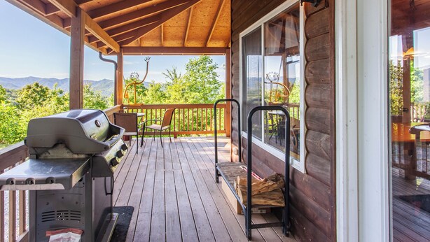 A wooden deck with a grill, chairs, and a view of mountains.