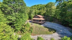 A cabin surrounded by dense forest with a gravel driveway leading to a covered porch.