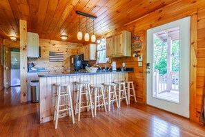 A wooden cabin interior with a kitchen, bar stools, and a door leading to an outdoor deck. - Escape to Goldies Hideaway (Bryson City)