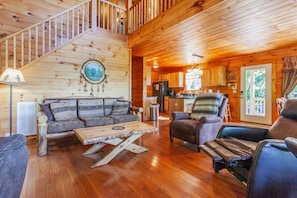A wooden cabin interior with a staircase, a sofa, a coffee table, and a kitchen area. - Escape to Goldies Hideaway (Bryson City)