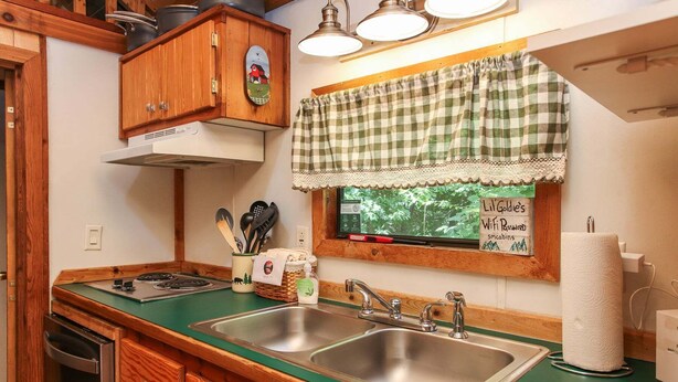 Cocina con gabinetes de madera, encimera verde, fregaderos de acero inoxidable y ventana con vistas a follaje.