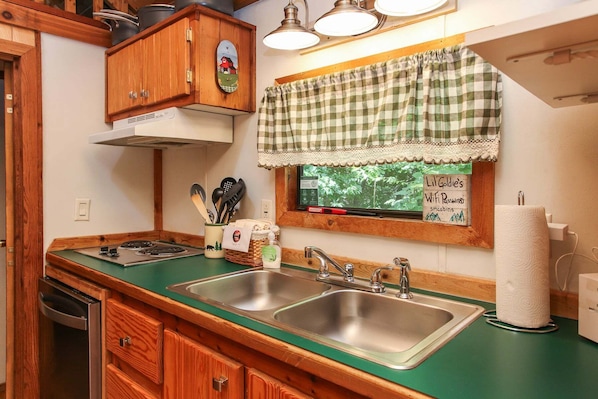 A kitchen with wooden cabinets, a green countertop, stainless steel sinks, and a window with a view of greenery.