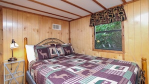 Una habitación con paneles de madera, una cama, una ventana con vistas a la vegetación y una lámpara.