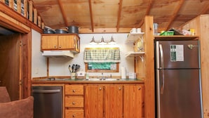 Una cocina compacta con armarios de madera, un refrigerador de acero inoxidable y un valance de ventana a cuadros.