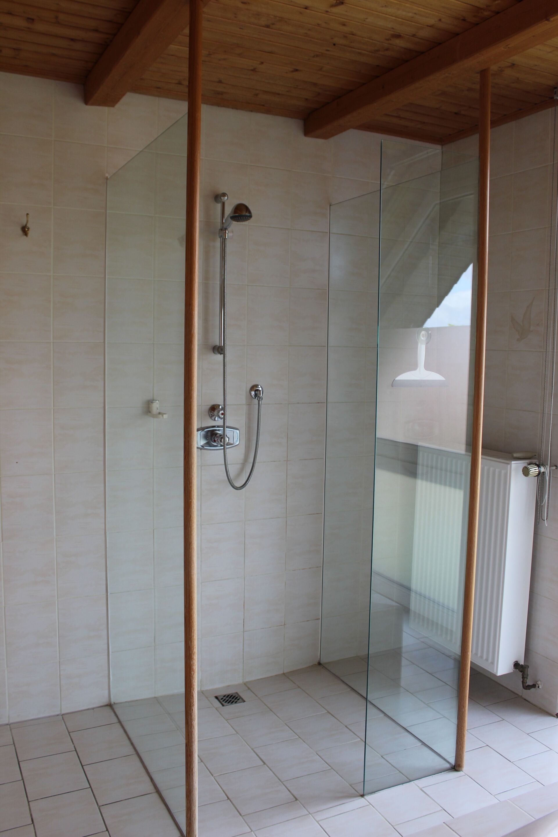 A glass-enclosed shower with a wooden ceiling, white tiled walls, and a visible radiator.