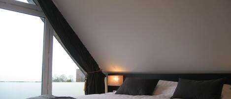A bedroom with a large window, a bed with a dark headboard, and a bedside lamp.