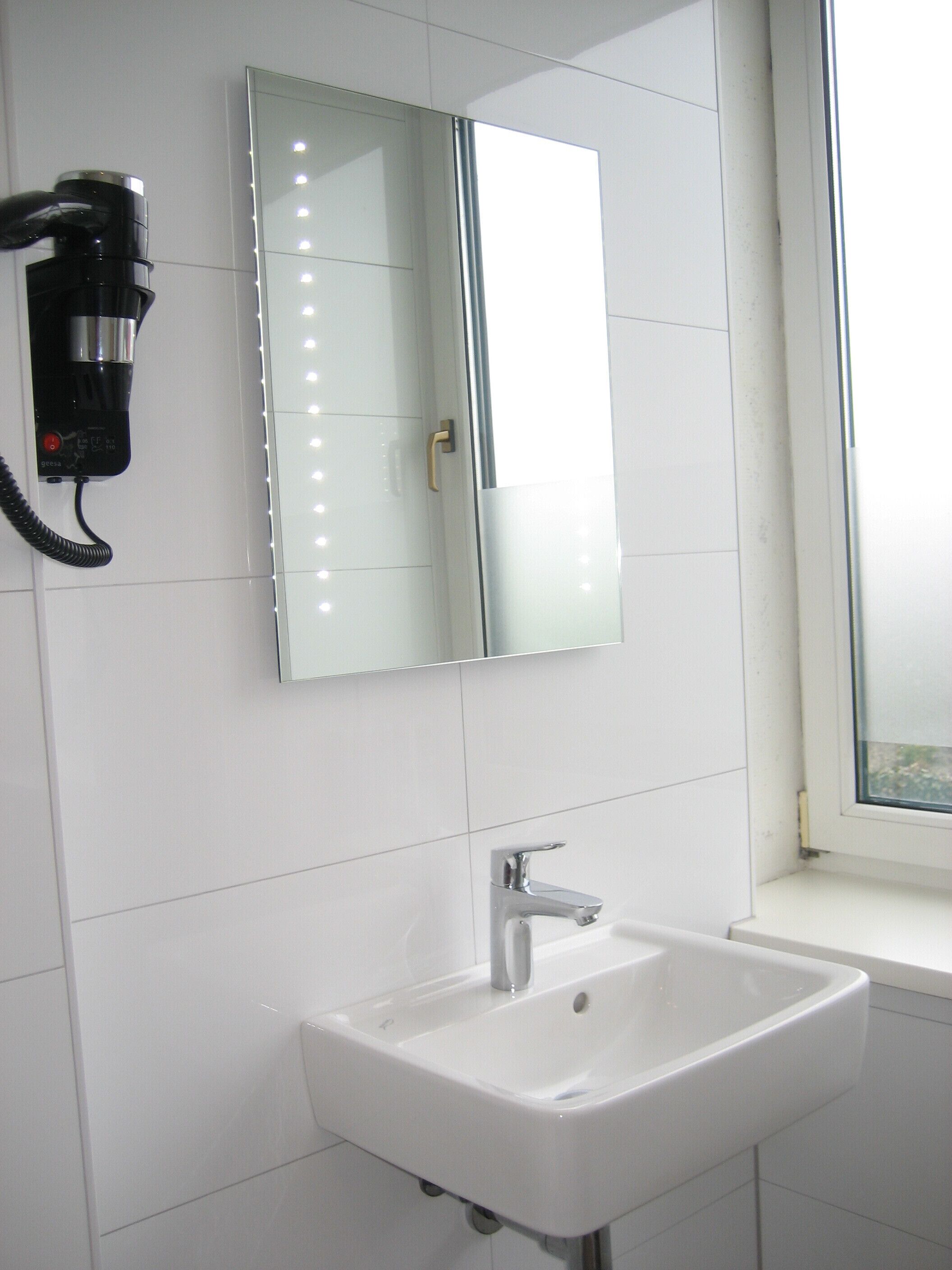 Un bagno con un lavandino bianco, uno specchio e un asciugacapelli montato a parete.