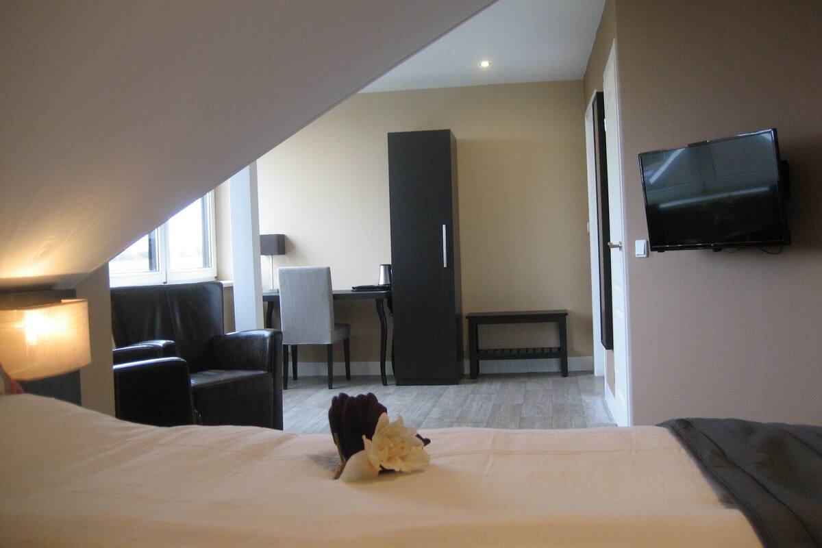 A hotel room with a bed, a desk, a chair, a TV, and a window.