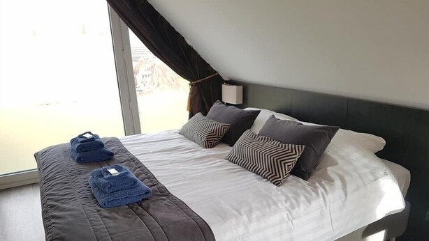 A modern hotel room with a large bed, a window with curtains, and a bedside table with a lamp. - Bed & Breakfast Rheiderland (Bunde)