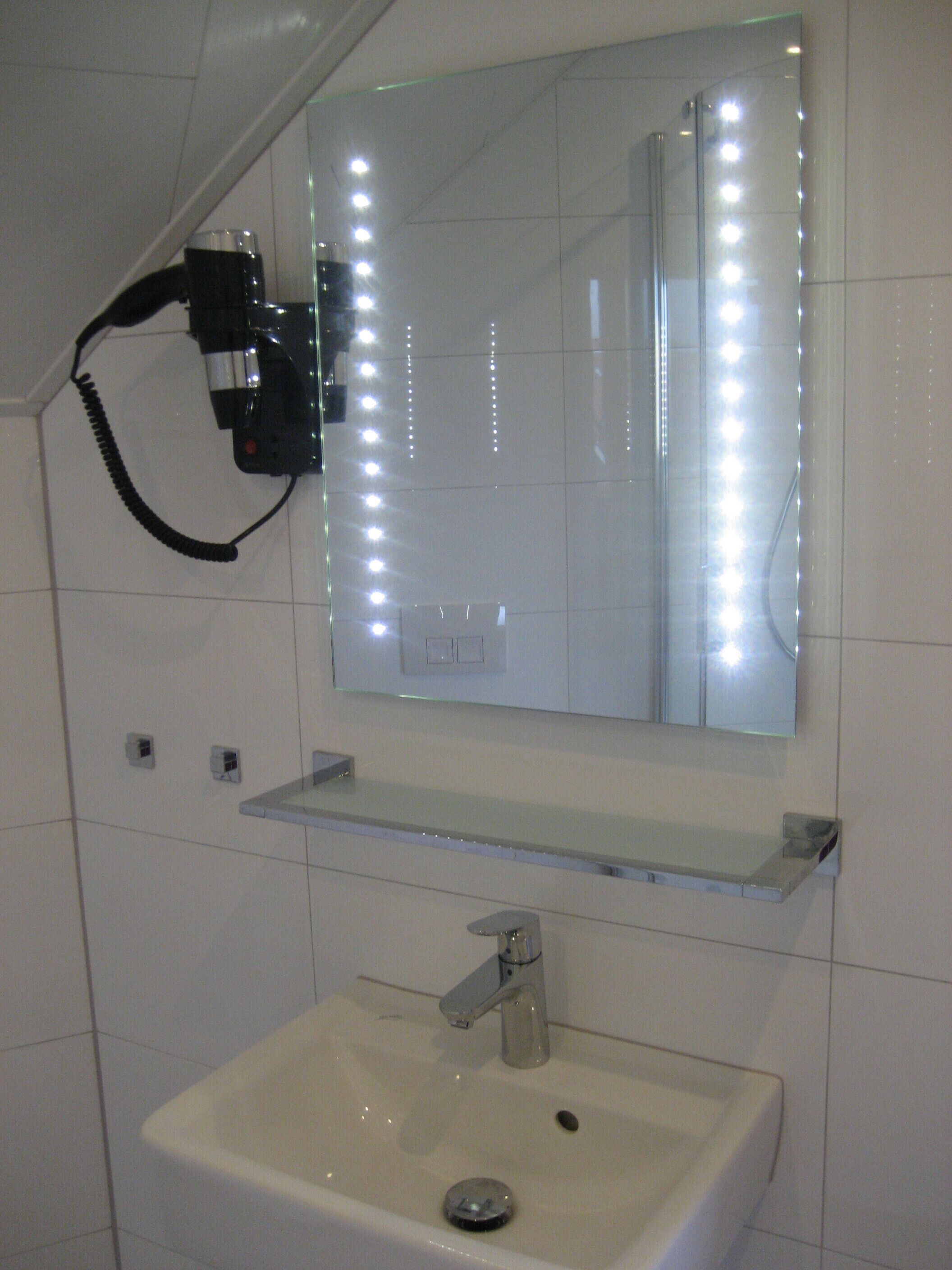 A bathroom with a white sink, a mirror with lights, and a hairdryer mounted on the wall.