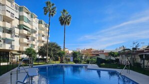 Piscina com grades de metal, cercada por um gramado bem cuidado e palmeiras.