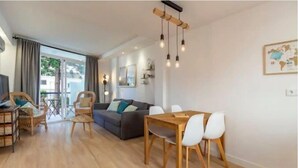 Uma sala de estar moderna com um sofá, mesa de jantar e cadeiras. Há uma janela grande com cortinas, piso de madeira e um lustre.
