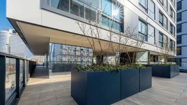 Un edificio moderno con amplios ventanales, una zona exterior cubierta y jardineras con plantas.