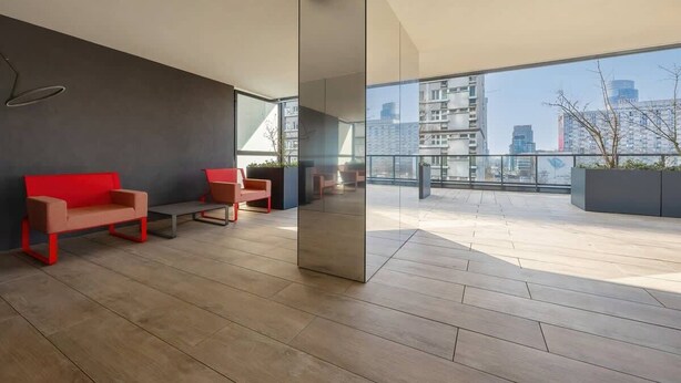 Un interior moderno con un amplio muro de vidrio, asientos de color rojo y marrón, y vistas a rascacielos.