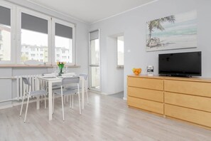 Un salon moderne comprenant un coin repas, un téléviseur et un tableau représentant une scène de plage.
