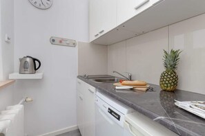 Une cuisine compacte équipée d’un lave-vaisselle, d’un évier et d’un plan de travail sur lequel se trouvent un ananas et une planche à découper.