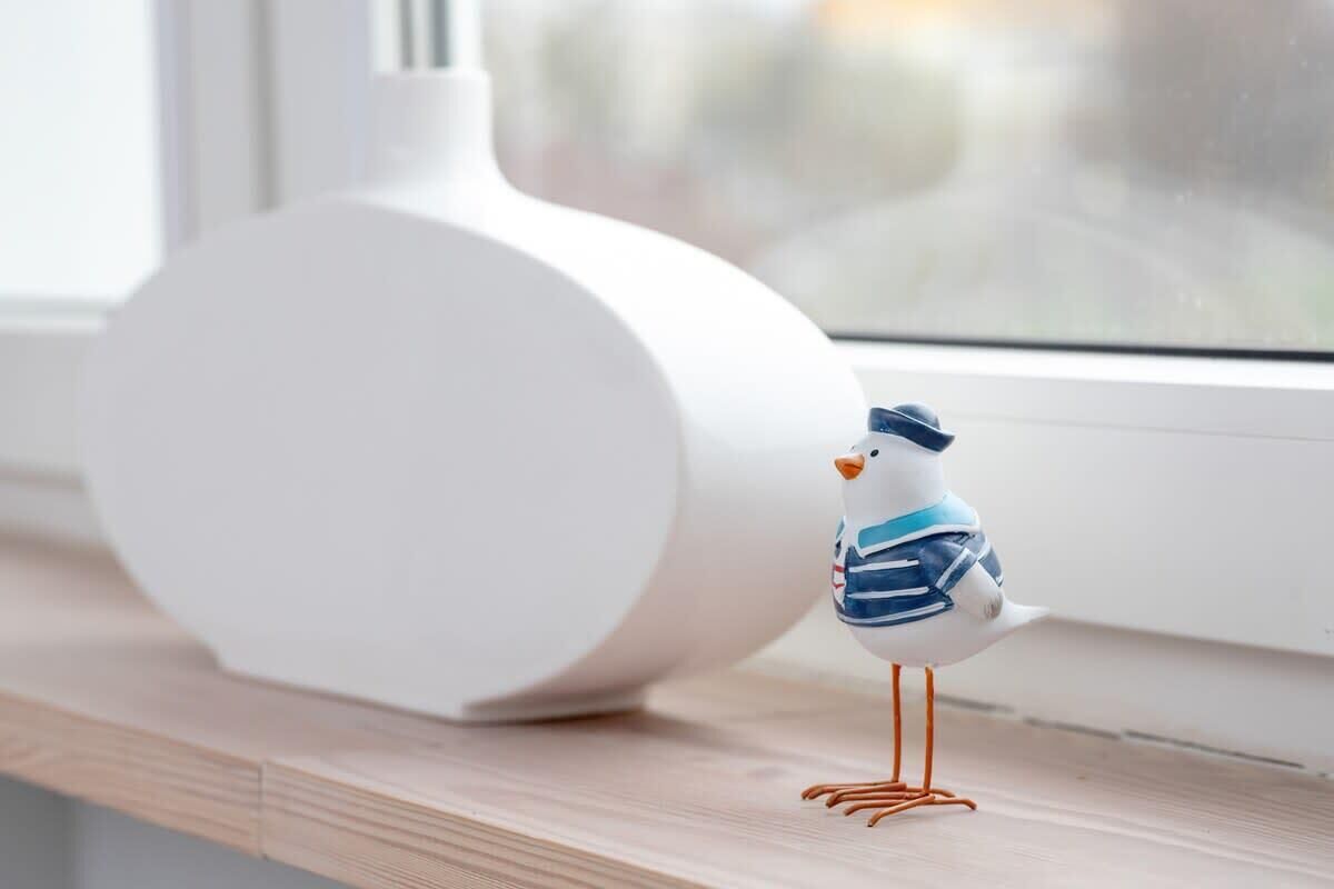 Eine Vogel-Figurine auf einer Holzablage neben einer weißen Vase.