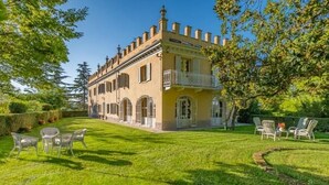 A large, two-story building with a balcony, surrounded by a well-maintained lawn and outdoor furniture. - Luxury Villa - Unesco Monferrato Langhe Roero with private pool (Asti)