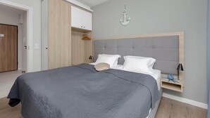 A bedroom with a large bed, a grey upholstered headboard, a wooden wardrobe, and a wall-mounted anchor decoration.