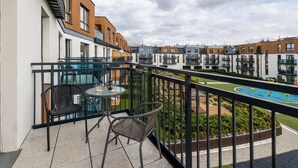 A balcony with two chairs and a table, overlooking a swimming pool and neighboring buildings.