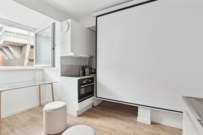 Et moderne køkken med stort vindue, hvide skabe, indbygget ovn og en lys bordplade.