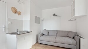A compact kitchen with a built-in sink, a grey sofa, and a white cabinet. - ID 412 - Beaugrenelle / rue Gaston de Caillavet (studio) (Paris)