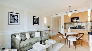 Un salon moderne avec un canapé gris, une table basse blanche et un coin repas comprenant des chaises en bois et une table blanche.