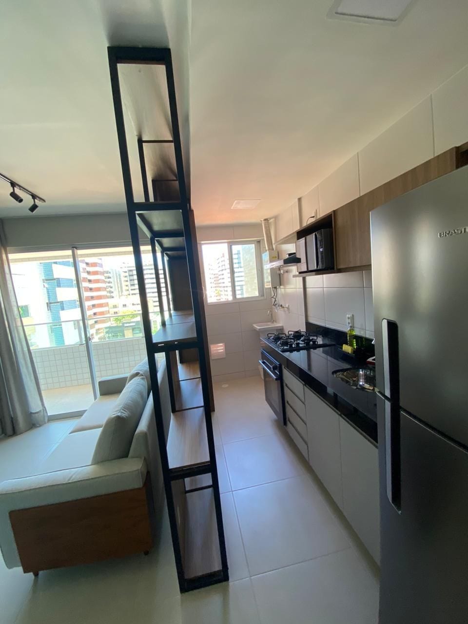 Una cocina moderna con refrigerador empotrado, estufa y microondas. Hay una ventana que ofrece luz natural y vistas de edificios.