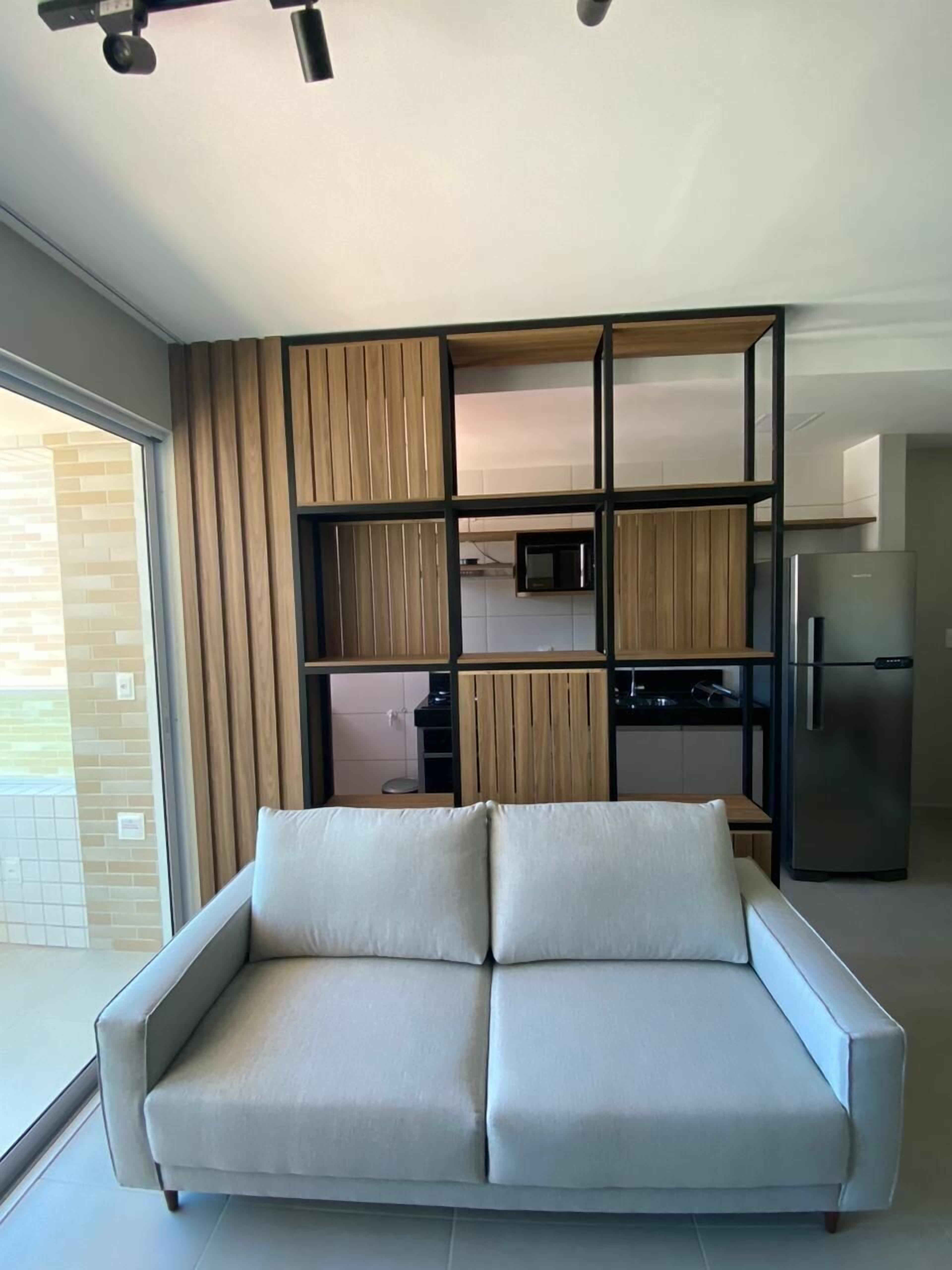 Un saló modern amb un sofà, una cuina amb microones i nevera, i una porta corredissa de vidre que dona a una zona exterior.