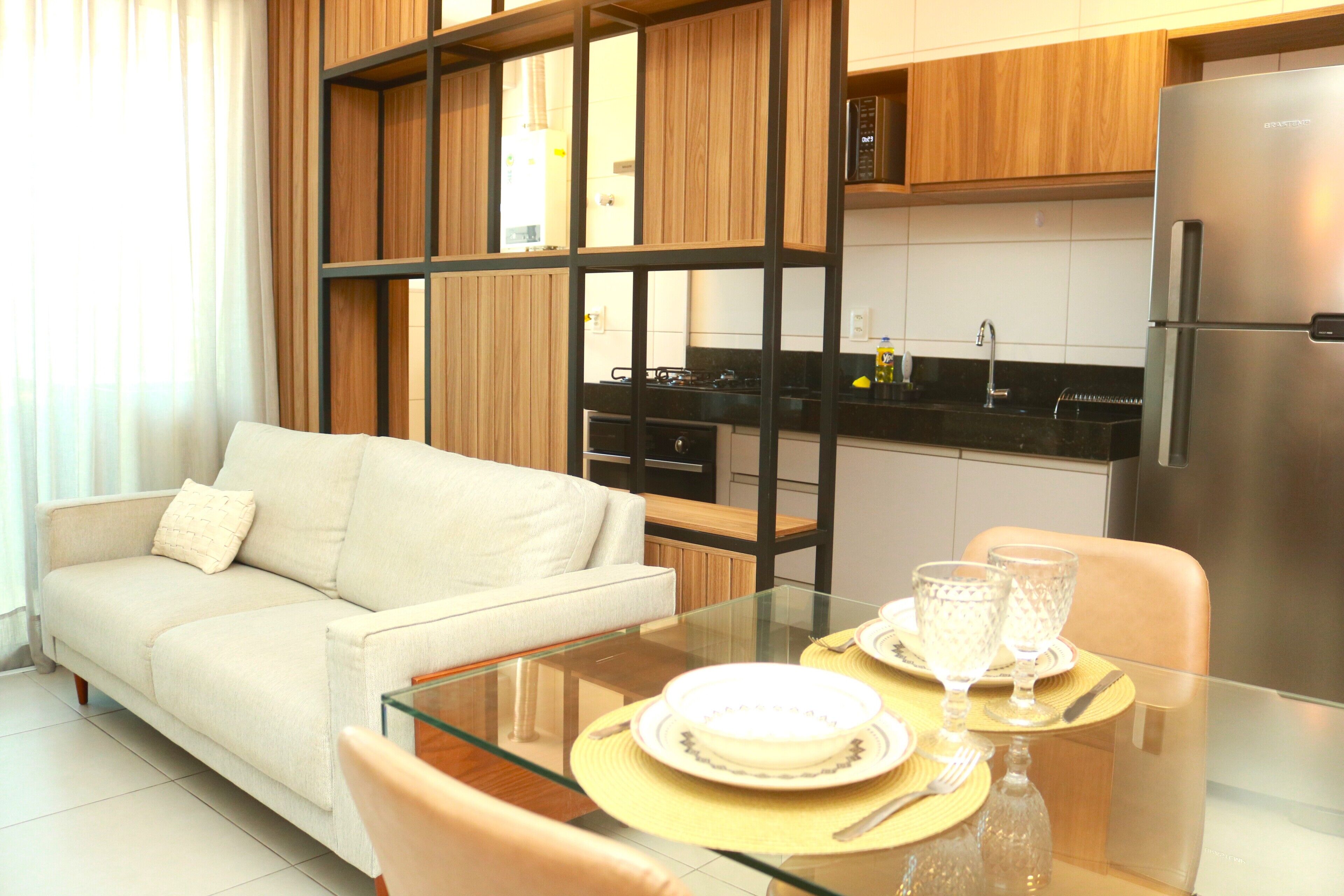 A modern kitchen with wooden cabinets, a stainless steel refrigerator, and a glass dining table set for two.