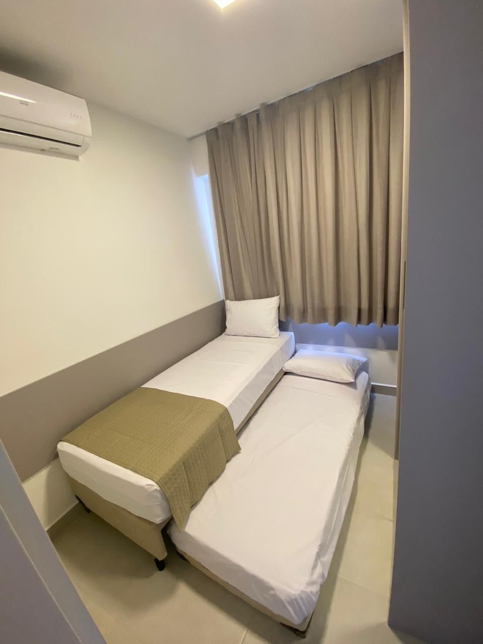 Habitación de hotel con dos camas, una ventana con cortinas, un equipo de aire acondicionado y un interruptor de luz en la pared.