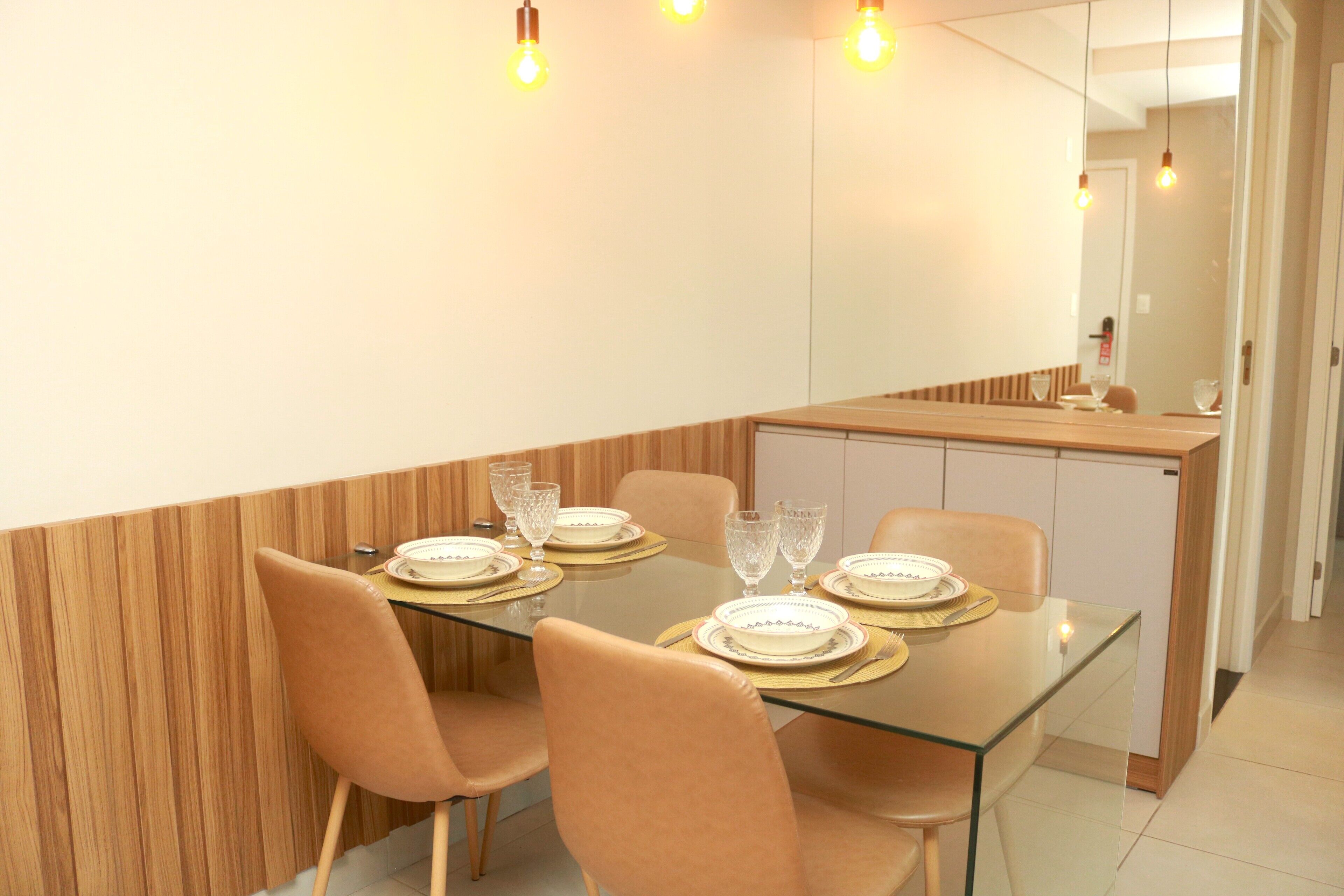 A modern dining area with a glass table, four cushioned chairs, and a wooden accent wall.