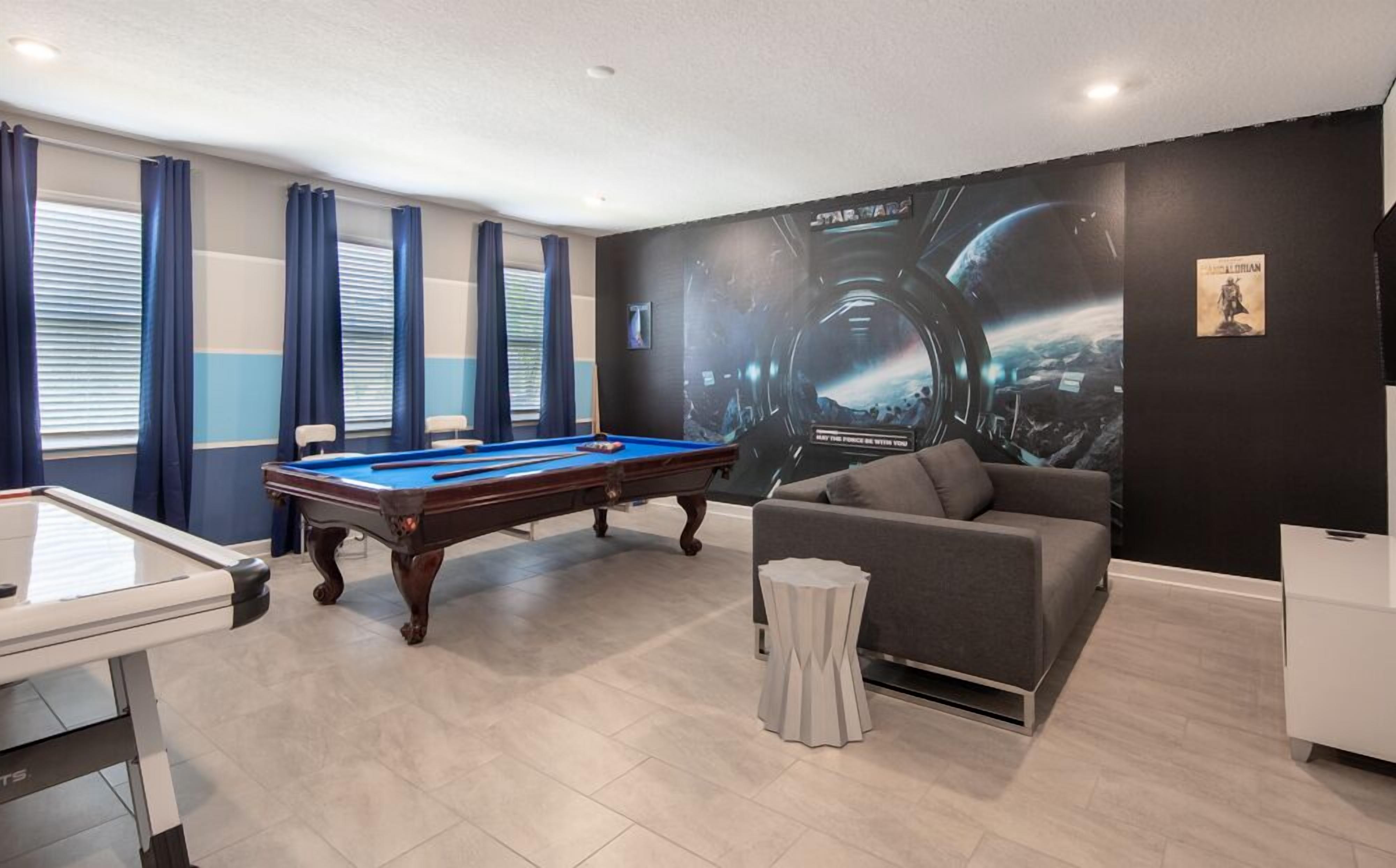 A pool table in a room with a large Star Wars mural, a sofa, and a small table.