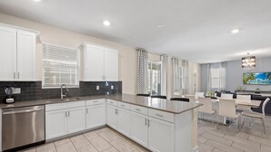 Une cuisine moderne avec des meubles blancs, un lave-vaisselle en acier inoxydable et un dosseret de carrelage noir.