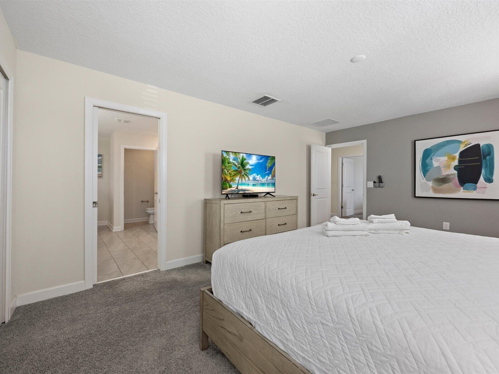 A bedroom with a large bed, a television on a dresser, and a painting on the wall.