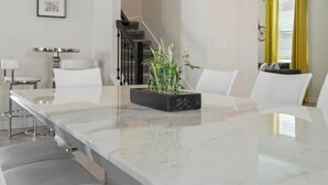 Un espace repas moderne avec une table en marbre, des chaises blanches et un arrangement floral décoratif en guise de centre de table.