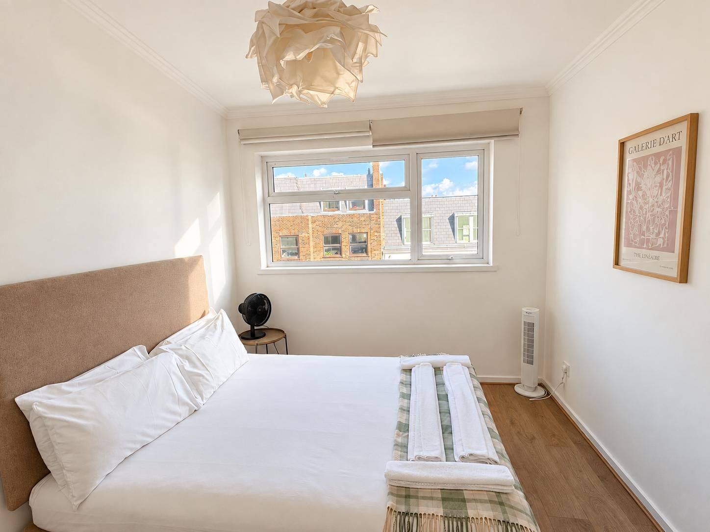 A bedroom with a bed, a window, a radiator, and a framed artwork on the wall.