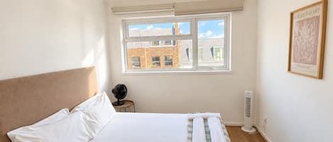A bedroom with a bed, a window, a radiator, and a framed artwork on the wall.