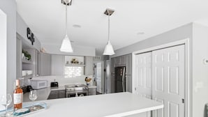 Une cuisine moderne avec des meubles blancs, un îlot central, des appareils en acier inoxydable et des luminaires suspendus.