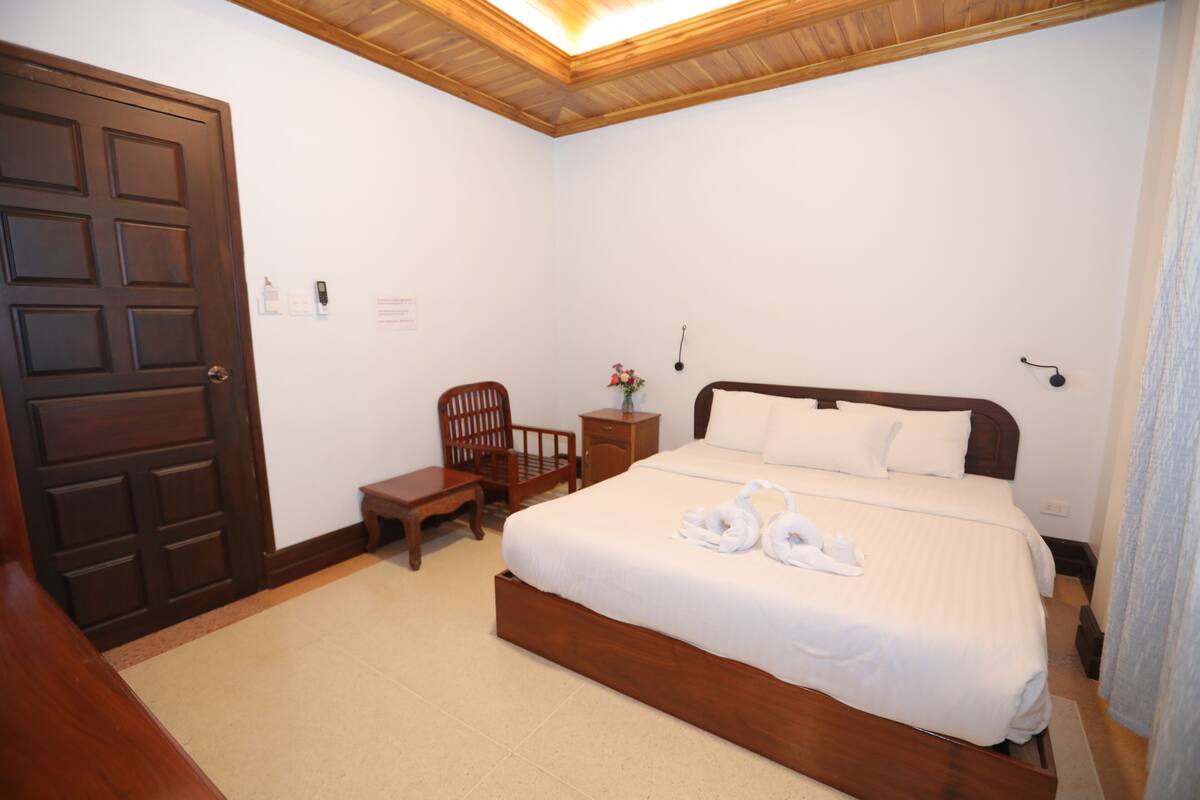 A bedroom with a wooden bed, a wooden chair, a nightstand, and a door.