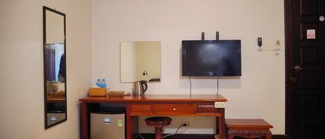 A compact room with a wooden desk, a small stool, a wall-mounted TV, a mirror, and a door.
