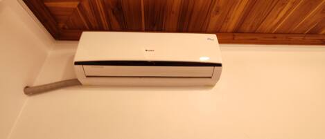 A white air conditioning unit mounted on a wall with a wooden ceiling above.