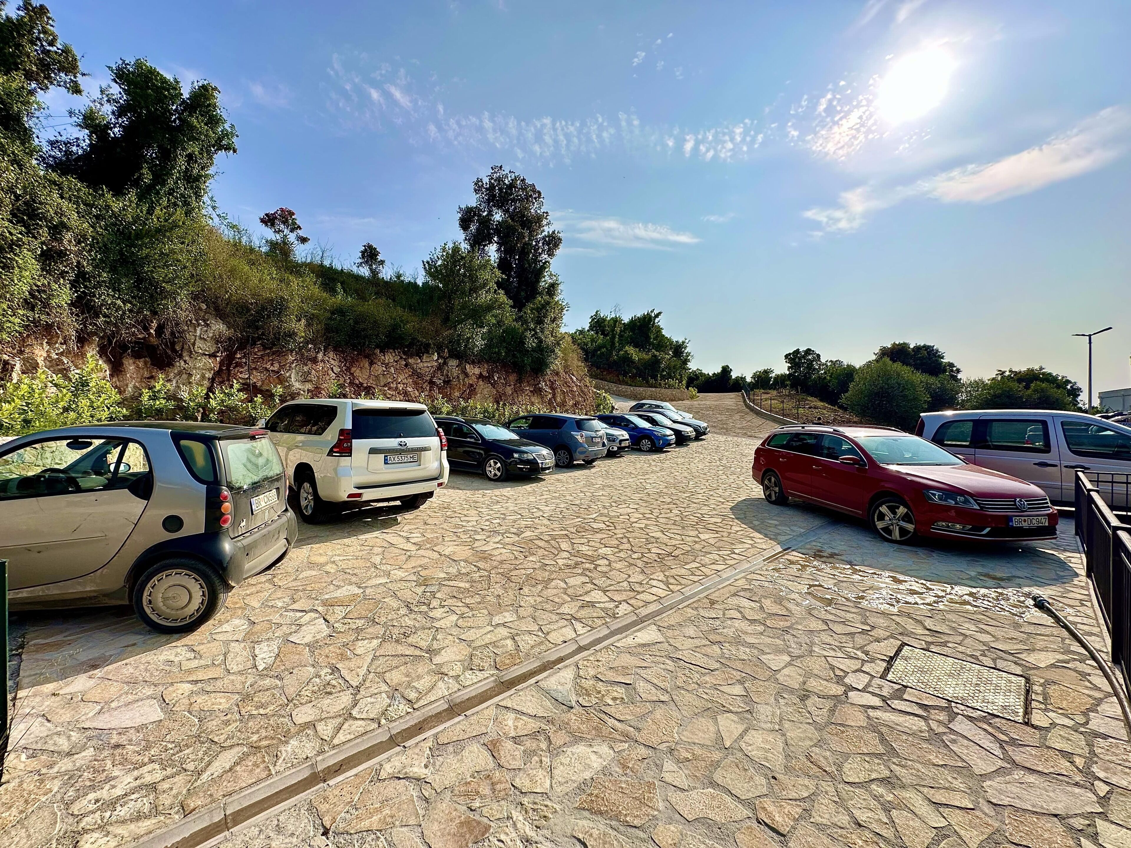 Ein Parkplatz mit mehreren Autos, befestigtem Pflasterboden und einer Steinmauer mit Bepflanzung.